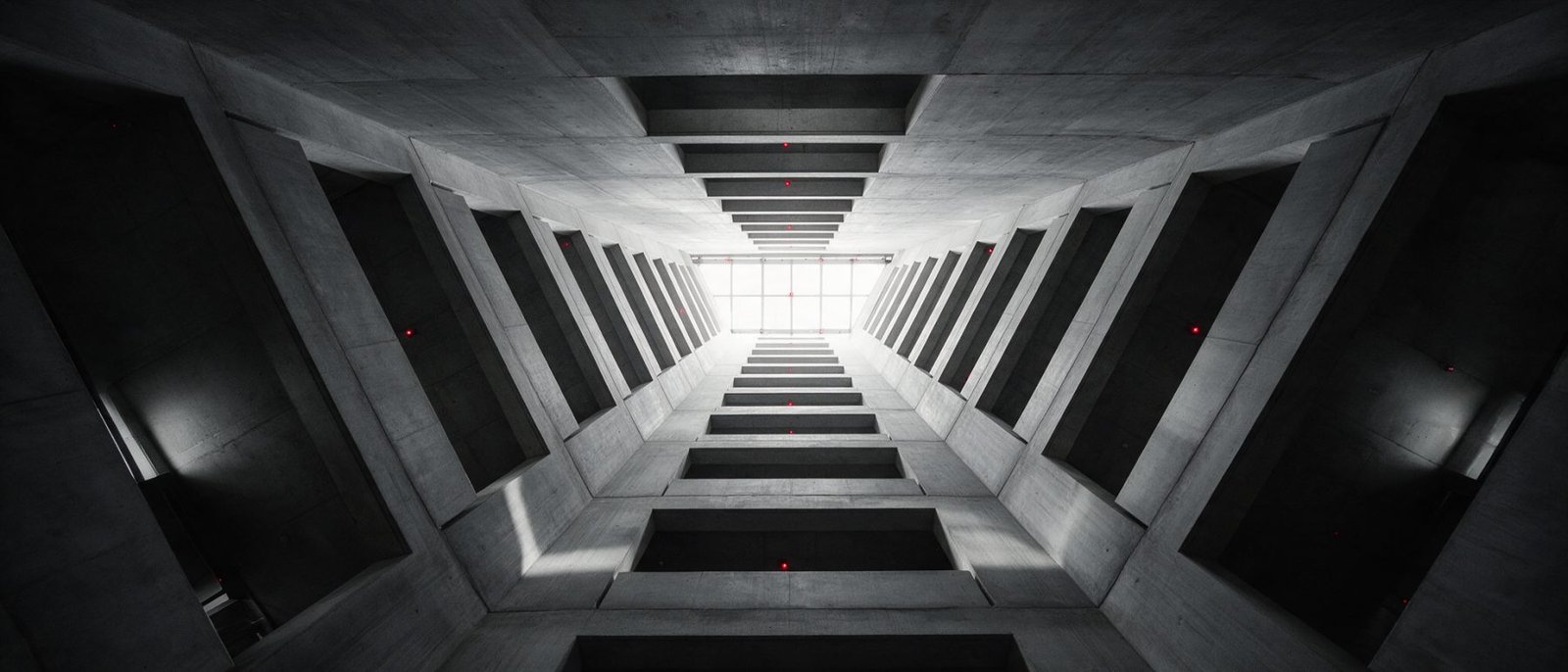 Looking up into a concrete atrium with stacked balcony openings receding toward a skylight