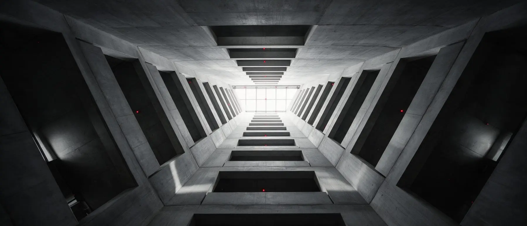 Looking up into a concrete atrium with stacked balcony openings receding toward a skylight