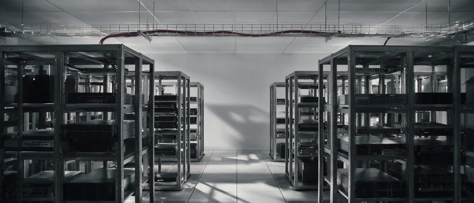 Systems integration UAE - Corporate server room seen down the central walkway, open rack frames on both sides under overhead cable tray