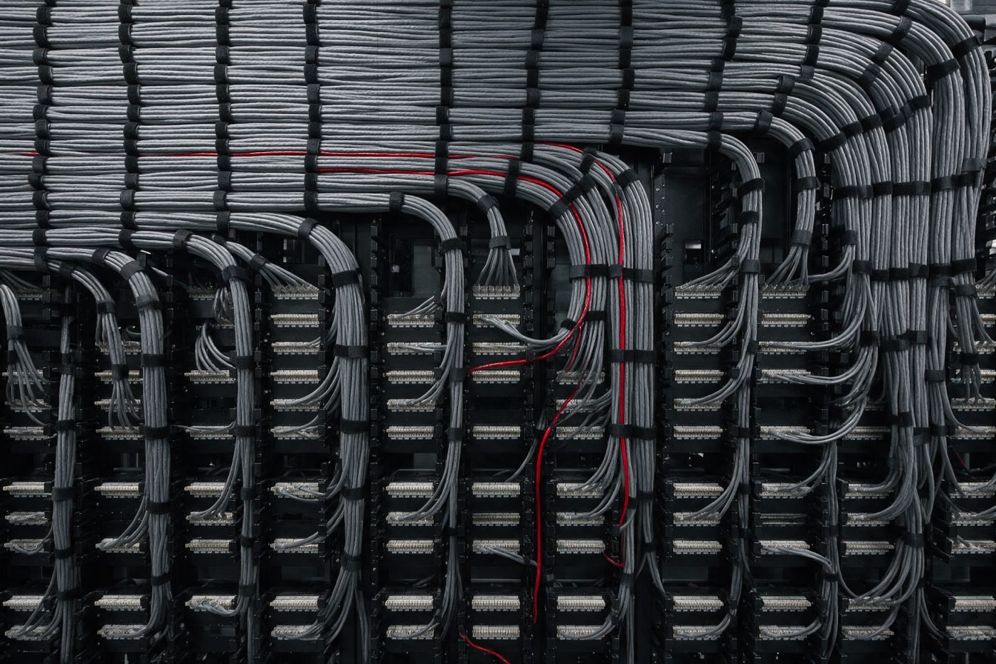 Structured cabling patch panel dressed in parallel runs, with a single red patch lead traced through the bundle
