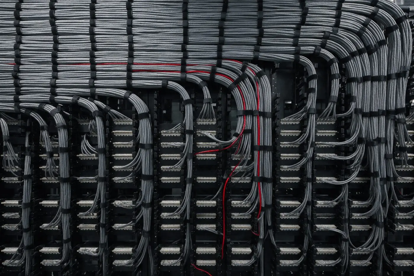 Structured cabling patch panel dressed in parallel runs, with a single red patch lead traced through the bundle
